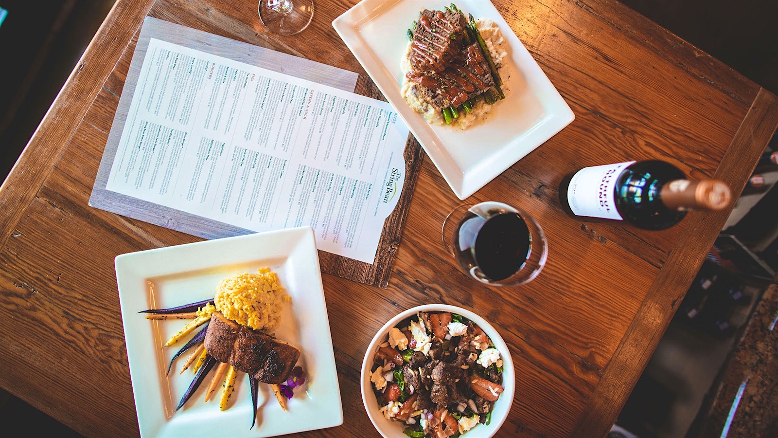 a selection of food, a menu, a glass of red wine and a bottle of red wine